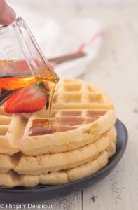 pouring maple syrup on stack of three gluten free Belgian waffles with sliced strawberry