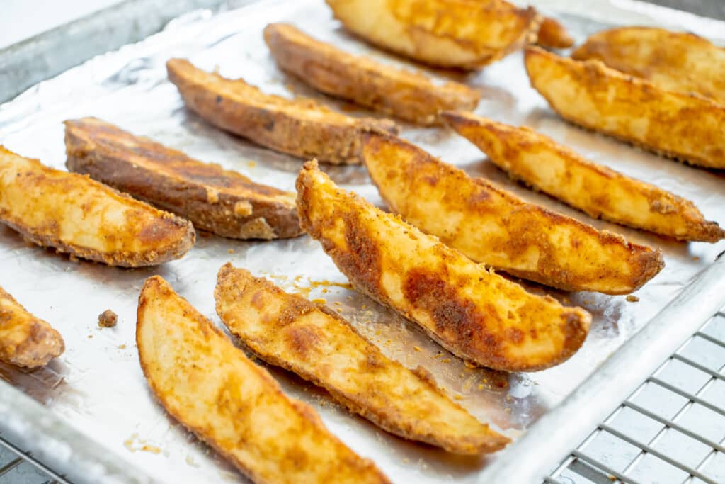crispy seasoned potato wedges lined up on a foil lined pan