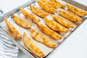 Pan of uncooked potato wedges to bake in the oven on a foil lined baking sheet