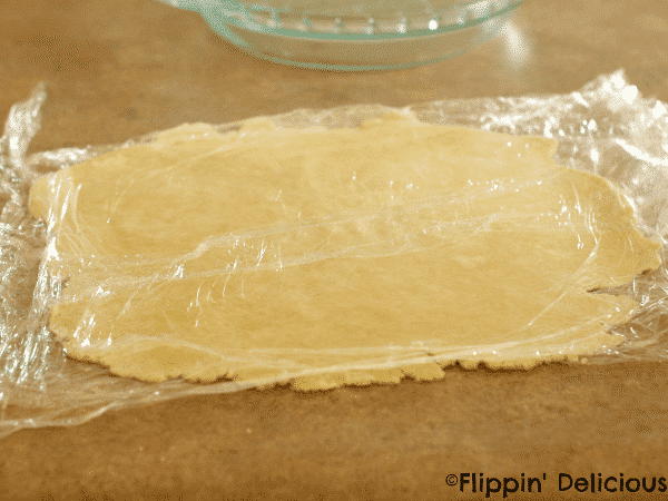 gluten free pie crust dough rolled out between two pieces of plastic wrap