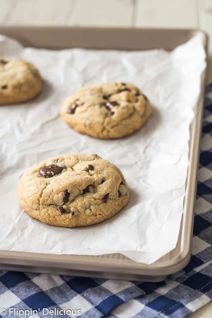 three gluten free chocolate chip cookies with golden edges on a baking sheet lined with white parchment paper