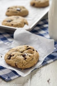 three gluten free chocolate chip cookies with golden edges on a baking sheet lined with white parchment paper