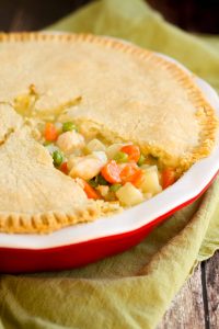gluten free chicken pot pie in a red ceramic pie dish ith a slice of gluten free pie crust removed so you can see the chicken, potato, carrots, and celery