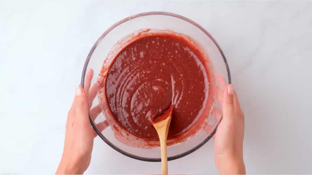 gluten free red velvet cake batter in a glass bowl with wooden spoon