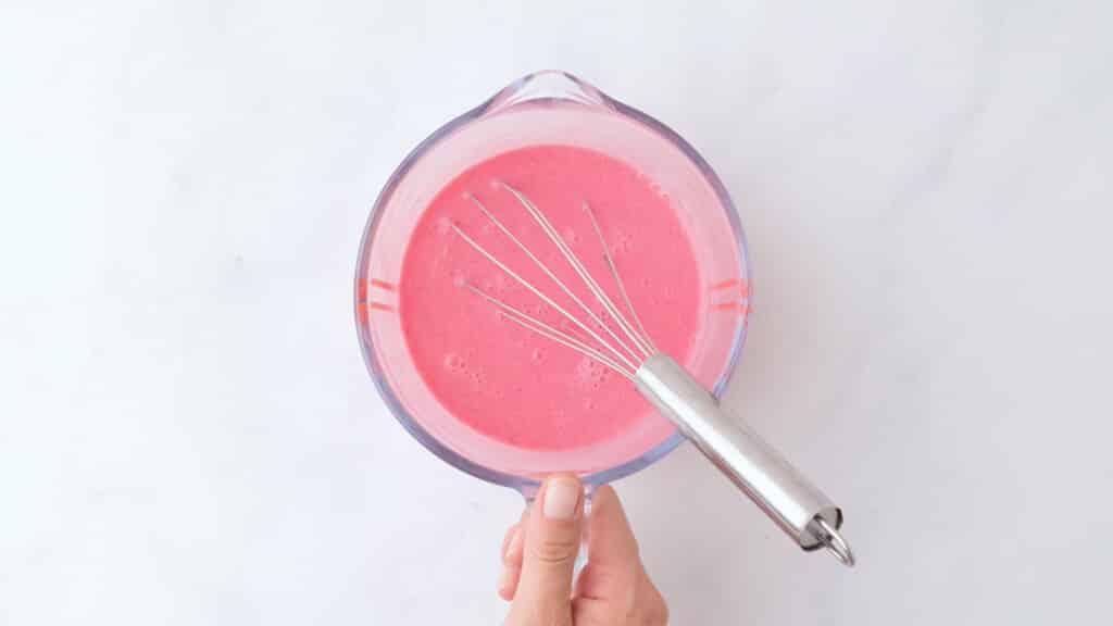 liquid ingredients for gluten free red velvet cake in a glass measuring cup with a silver whisk