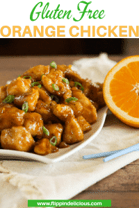 gluten free orange chicken on a white plate, beside a pair of blue chopsticks and a white napkin, garnished with green onions, with a half of an orange, with text "gluten free orange chicken"