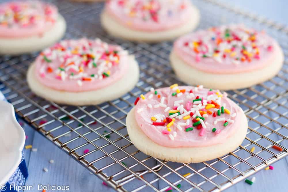 gluten free sugar cookies with pink icing and rainbow jimmies on a cooling rack
