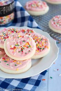 gluten free sugar cookies with pink frosting and rainbow sprinkles on a white plate