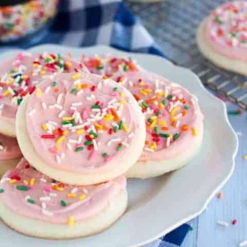 gluten free sugar cookies with pink frosting and rainbow sprinkles on a white plate