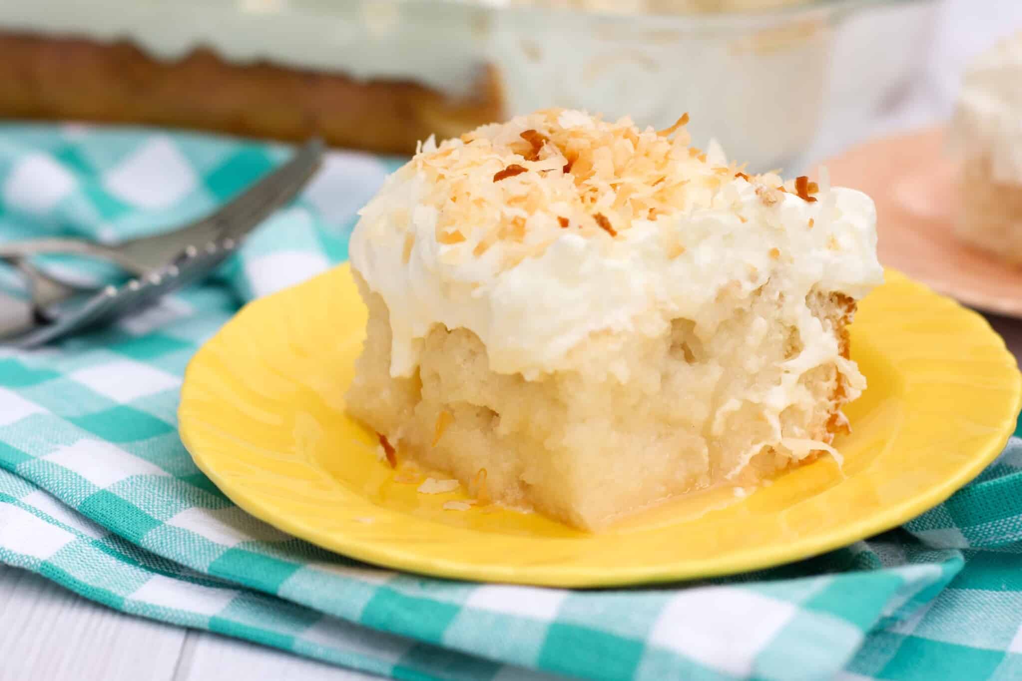 slice of gluten free poke cake with cream of coconut and toasted coconut on a yellow plate.