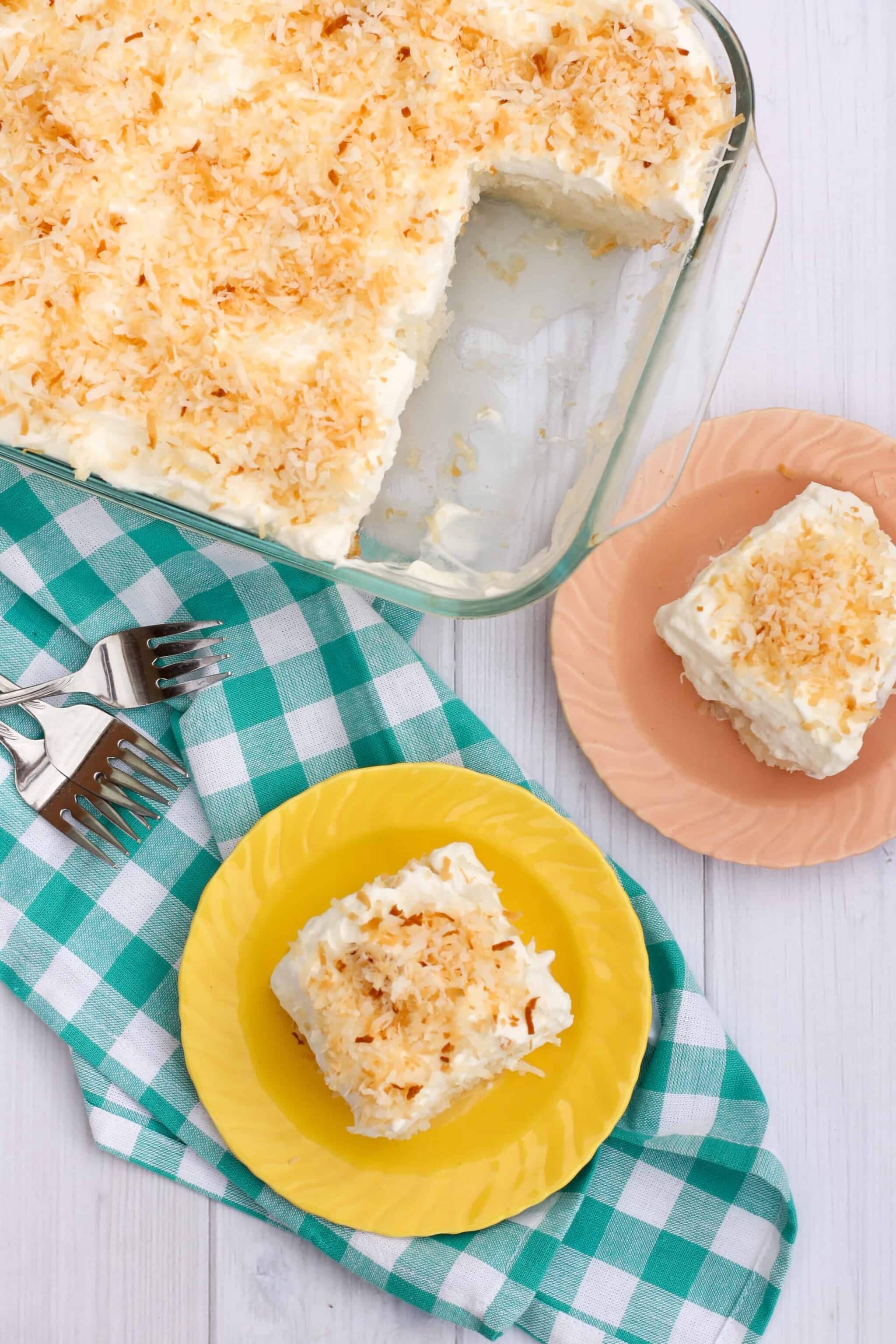 Overhead shot of coconut poke cake in a glass baking dish, with two slices removed and places on pastel plates.