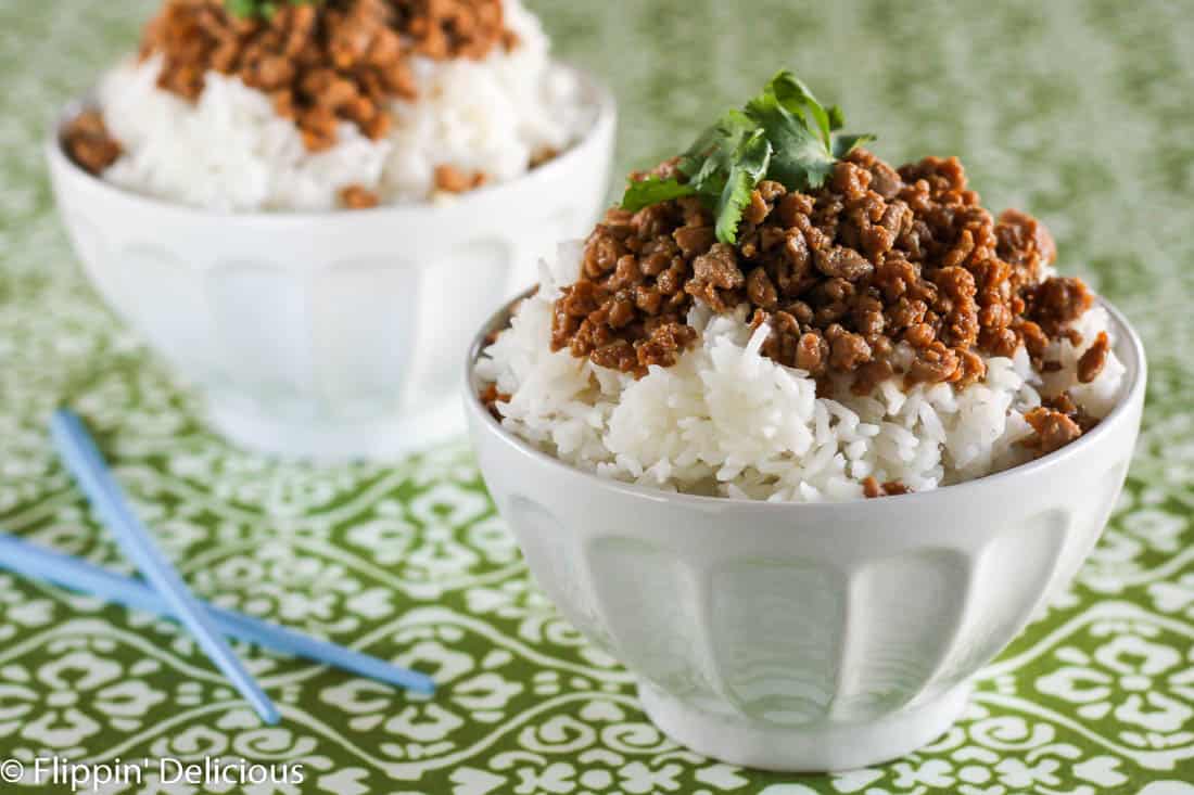 white bowl filled with rice and ground turkey seasoned with tamari and brown sugar, garnished with cilantro , on a green and white table cloth with blue chopstick beside the bowl