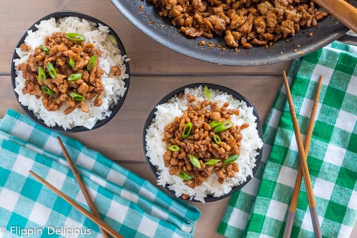 overhead view of two bowls filled with rice and gluten free korean ground turkey garnished with green onions and a nonstick skillet filled with more gluten free korean ground turkey