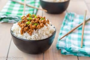 black bowl filled with rice topped with gluten free korean ground turkey garnished with green onions on a wooden table with teal and green napkins and wooden chopsticks