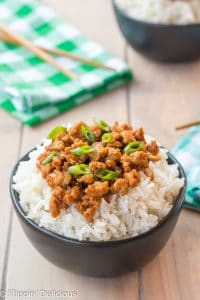 black matte bowl of rice topped with gluten free korean ground turkey garnished with green onions on a wooden table with teal and green napkins and wooden chopsticks