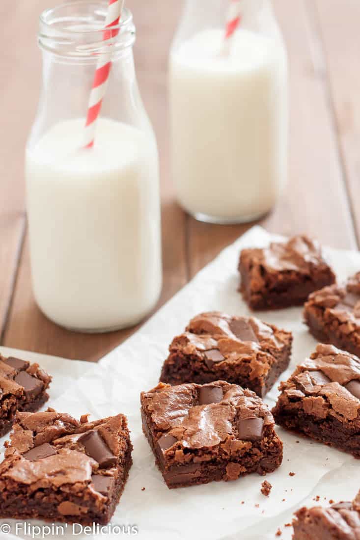 almond flour brownies with chocolate chunks cut into squares on a piece of parchment paper with two classic milk bottles with straws in the background