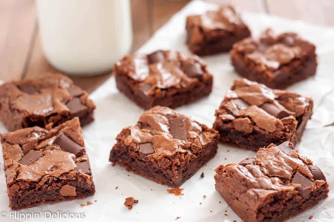 gluten free almond flour brownies with chocolate chunks cut into squares on a piece of parchment paper on a wooden table with a classic milk bottles in the background