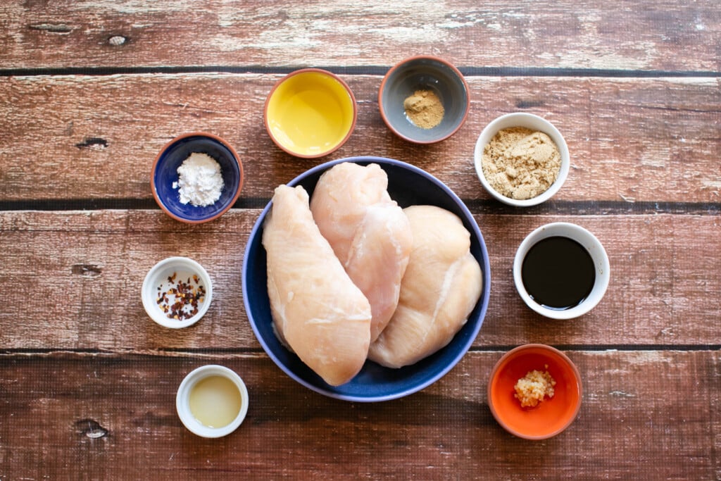 gluten free teriyaki chicken ingredients in small bowls on a wooden table, garlic, ginger, gluten free soy sauce, cornstarch, vinegar, brown sugar, red pepper flakes, and sesame oil