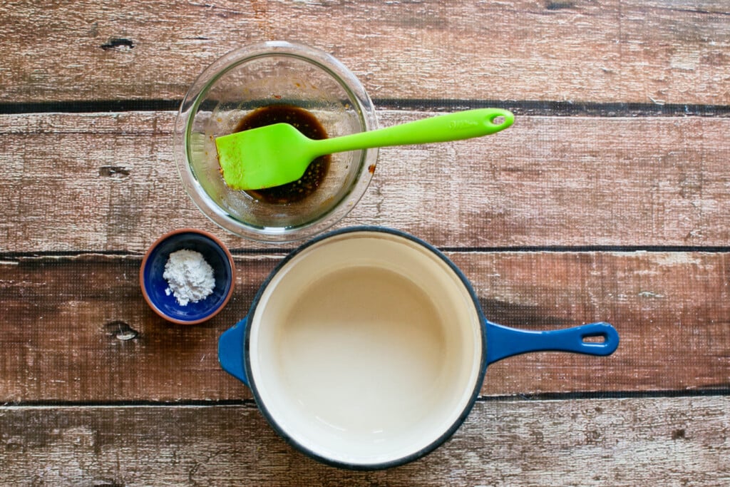 small bowl with cornstarch and small bowl with teriyaki marinade with a blue enamel saucepan