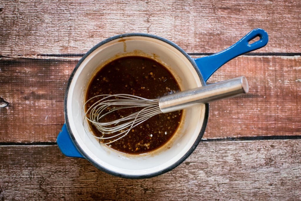 whisk mixing gluten free teriyaki sauce in a blue saucepan on a wooden table