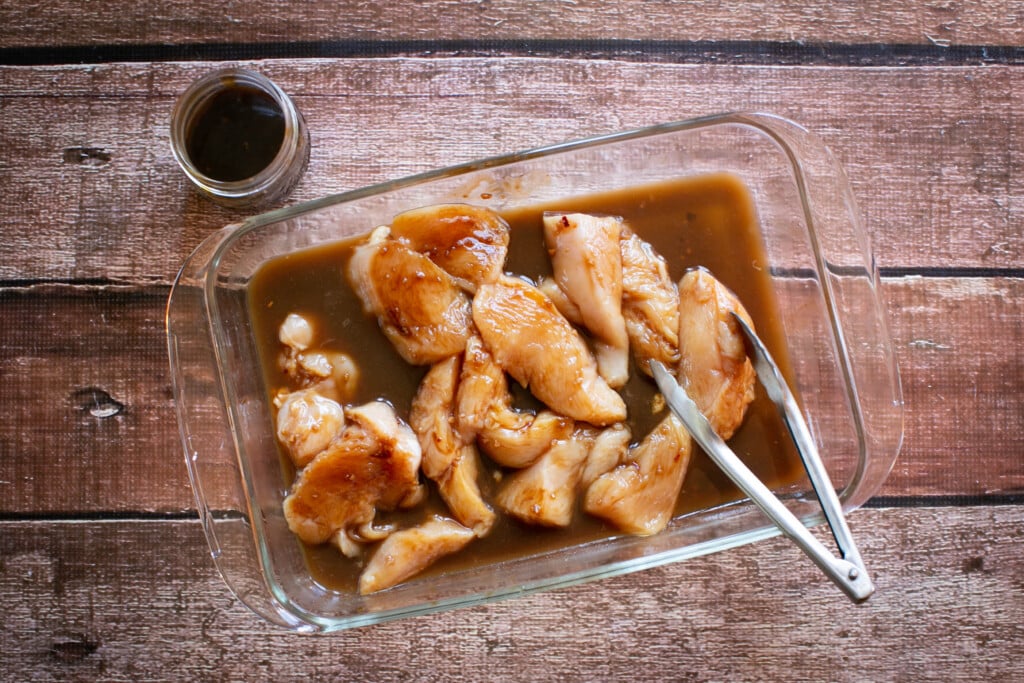 glass pan full of raw chicken marinated in gluten free teriyaki sauce ready for the grill