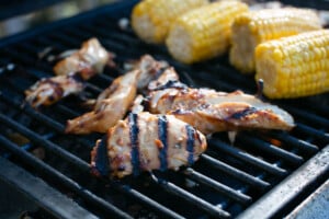 gluten free teriyaki chicken with grill marks on a grill with corn on the cob in the background
