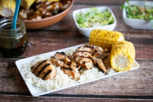 gluten free teriyaki chicken on a platter of rice with grilled corn on the cob