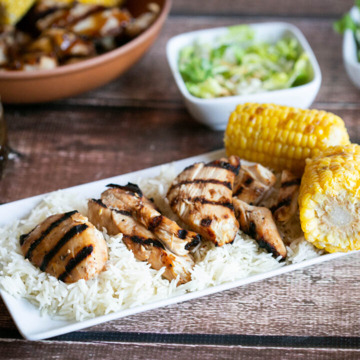 gluten free teriyaki chicken on a platter of rice with grilled corn on the cob