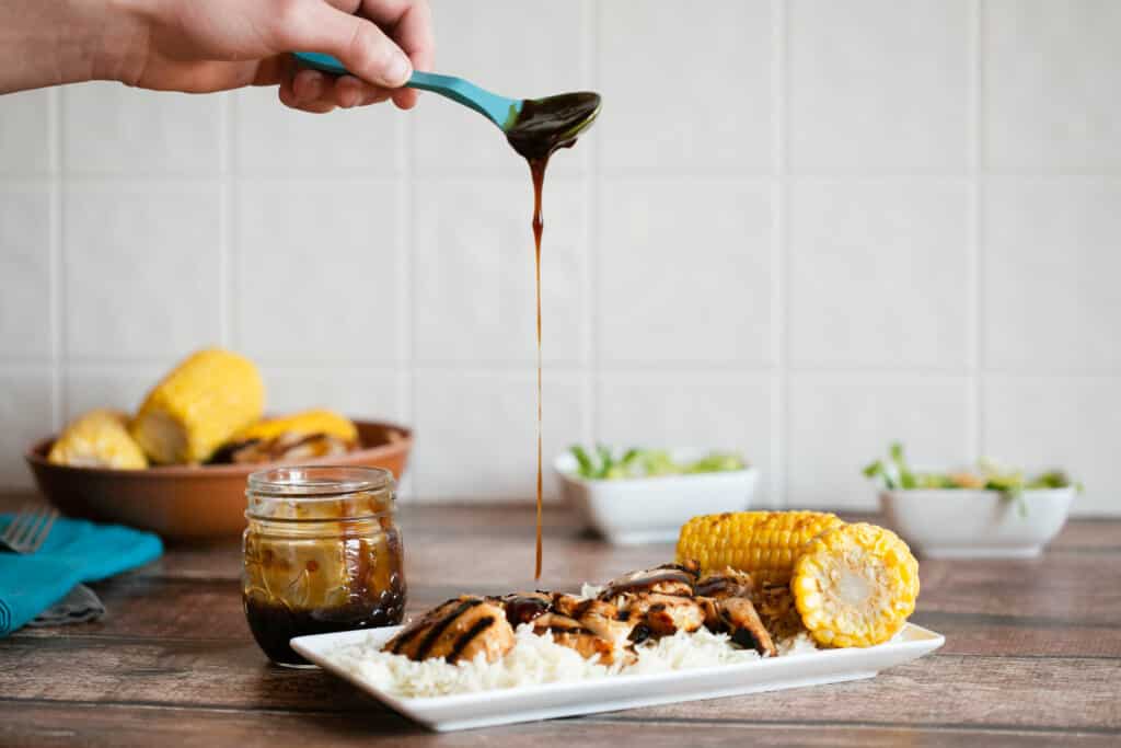 blue spoon pouring gluten free teriyaki sauce over grilled gluten free teriyaki chicken