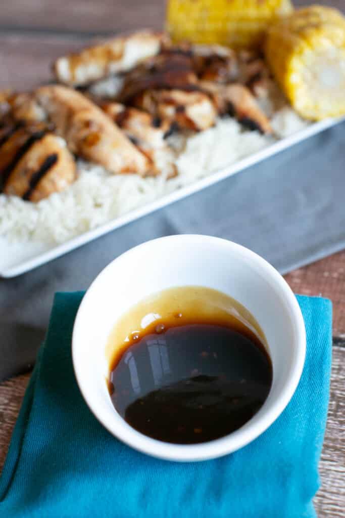 gluten free teriyaki sauce in a small white dish with gluten free grilled teriyaki chicken in the background on a bed of rice on a white platters 