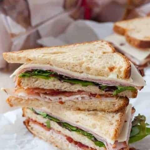 gluten free club sandwich with bacon, turkey, ham, canyon gluten free bread, cut in half on the diagonal and stack on top of each other