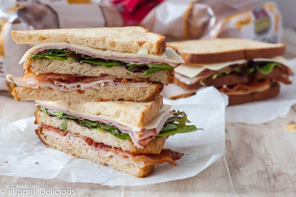 Glutenfreies Club-Sandwich mit Speck, Truthahn, Schinken, glutenfreiem Canyon-Brot, diagonal halbiert und übereinander gestapelt