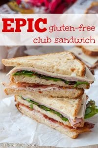 a big gluten free club sandwich made with three slices of bread, turkey, ham, bacon, swiss cheese, and spring mix cut in half on the diagonal and stacked on top of each other