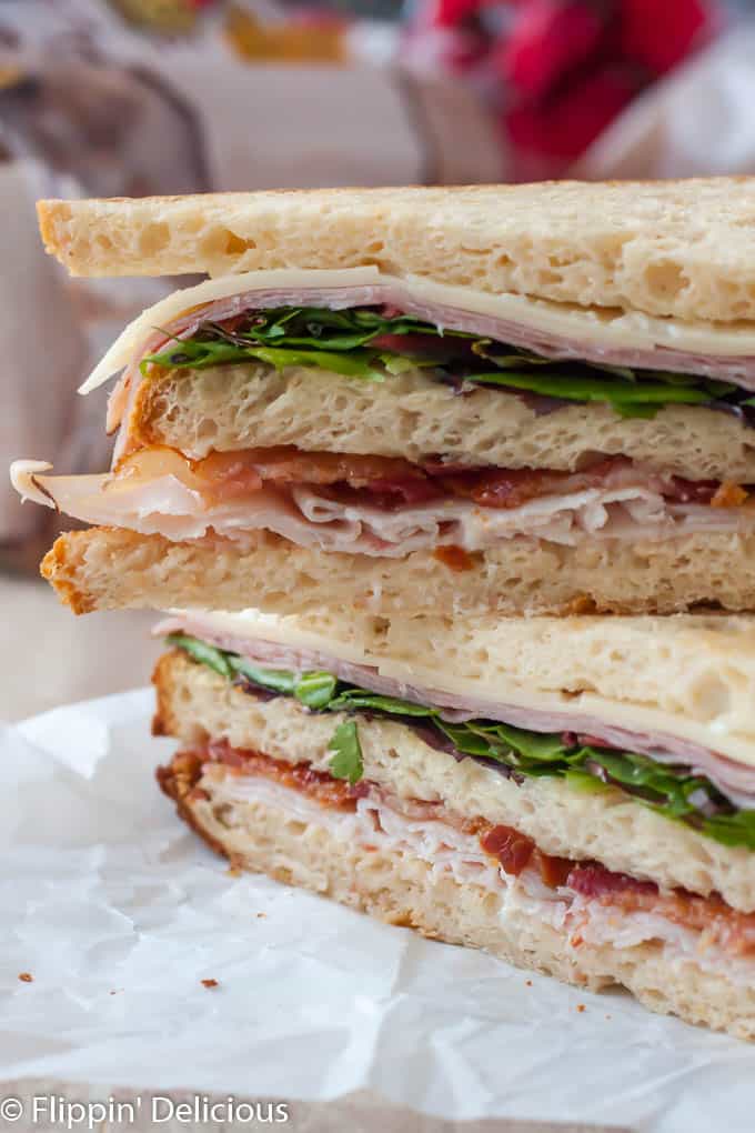   gluten free club sandwich with bacon, turkey, ham, canyon gluten free bread, cut in half on the diagonal and stack on top of each other