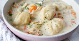 white bowl with gluten free chicken and dumpling soup with carrots and peas and potatoes with a spoon scooping in
