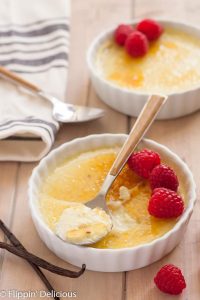 dairy free creme brulee with raspberries in a ramekin with a spoon on a wooden table