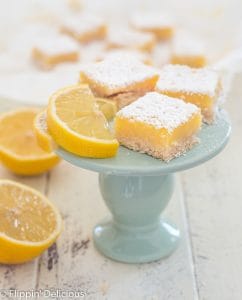 three gluten free lemon bars sprinkled with powdered sugar next to lemon slice on blue plate