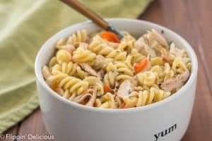 Instant Pot gluten free chicken noodle soup with carrots and rotisserie chicken in white bowl with wooden handle spoon