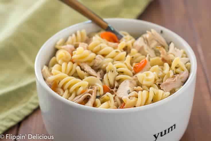 Instant Pot gluten free chicken noodle soup with carrots and rotisserie chicken in white bowl with wooden handle spoon 