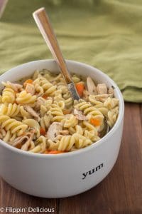 Instant Pot chicken noodle soup with gluten free pasta, sliced carrots, and herbes de Provence, in white bowl with wood handle spoon