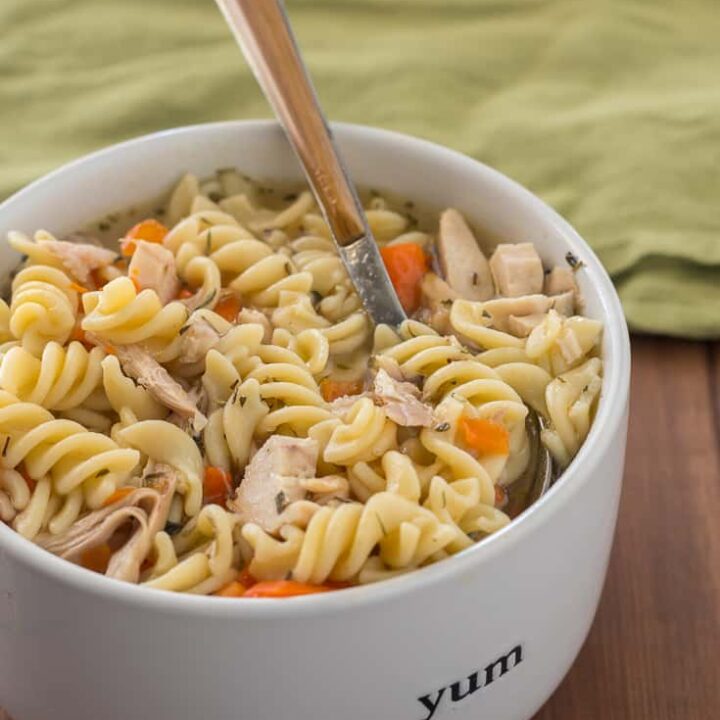 Instant Pot chicken noodle soup with gluten free pasta, sliced carrots, and herbes de Provence, in white bowl with wood handle spoon