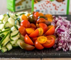 sliced cucumber, halved orange red and purple cherry tomatoes, and diced red onion on black cutting board