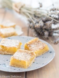 three gluten free lavender lemon bars on a blue plate with a bouquet of dried lavender in the background