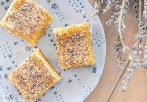 three gluten free lavender lemon bars on a blue plate beside a bouquet of dried lavender