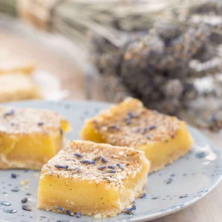 gluten free lavender lemon bars on a blue plate sprinkled with lavender buds with a bouquet of dried lavender in the background