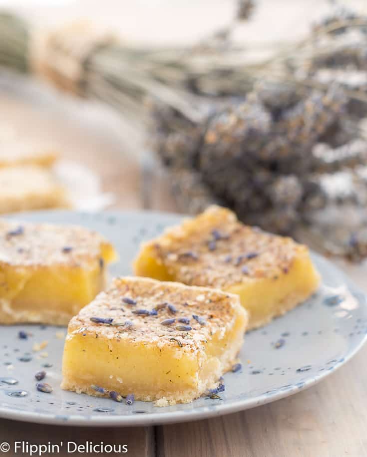 gluten free lavender lemon bars on a blue plate sprinkled with lavender buds with a bouquet of dried lavender in the background