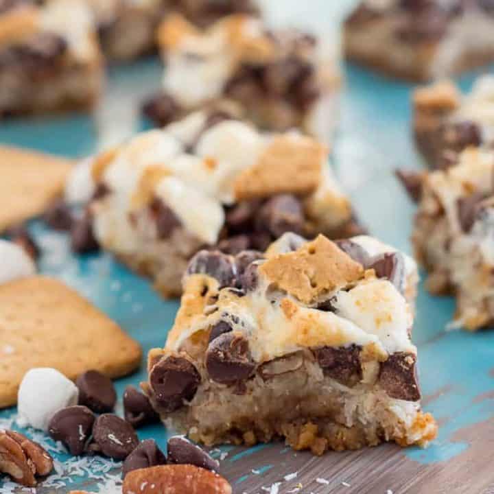 vegan gluten free magic cookie bars with marshmallows on a teal and gray table with schar honeygrams, pecans, chocolate chips, and marshallows