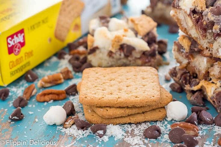 stack of schar honeygrams with marshmallows, chocolate chips, pecans, and shredded coconut with vegan gluten free magic cookie bar in the background