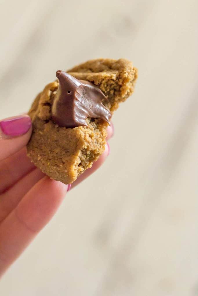 hand with pink manucure holding a Gluten free blossom cookies topped with a melty hershey's kiss with a bite take out of it.