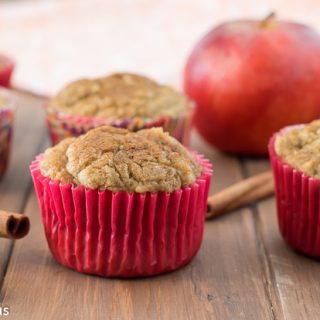 gluten free apple cinnamon muffins on a wooden table with cinnamon sticks, an apple and a dish towel in the background